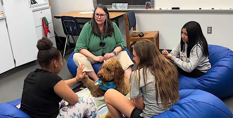 Dr. Larson and her student are sitting with Winston the therapy dog. 